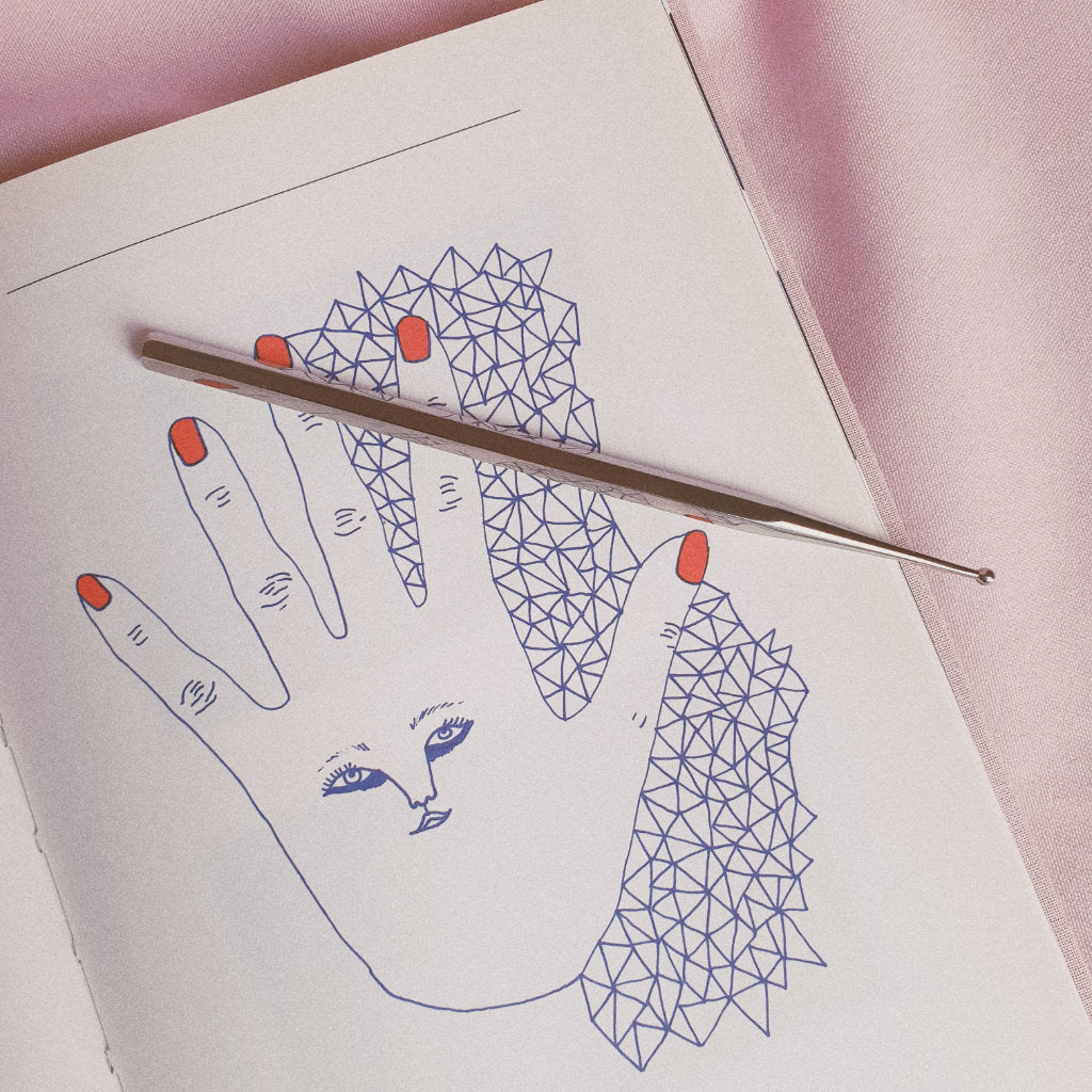 Stainless steel facial reflexology tool on a book with hand drawing