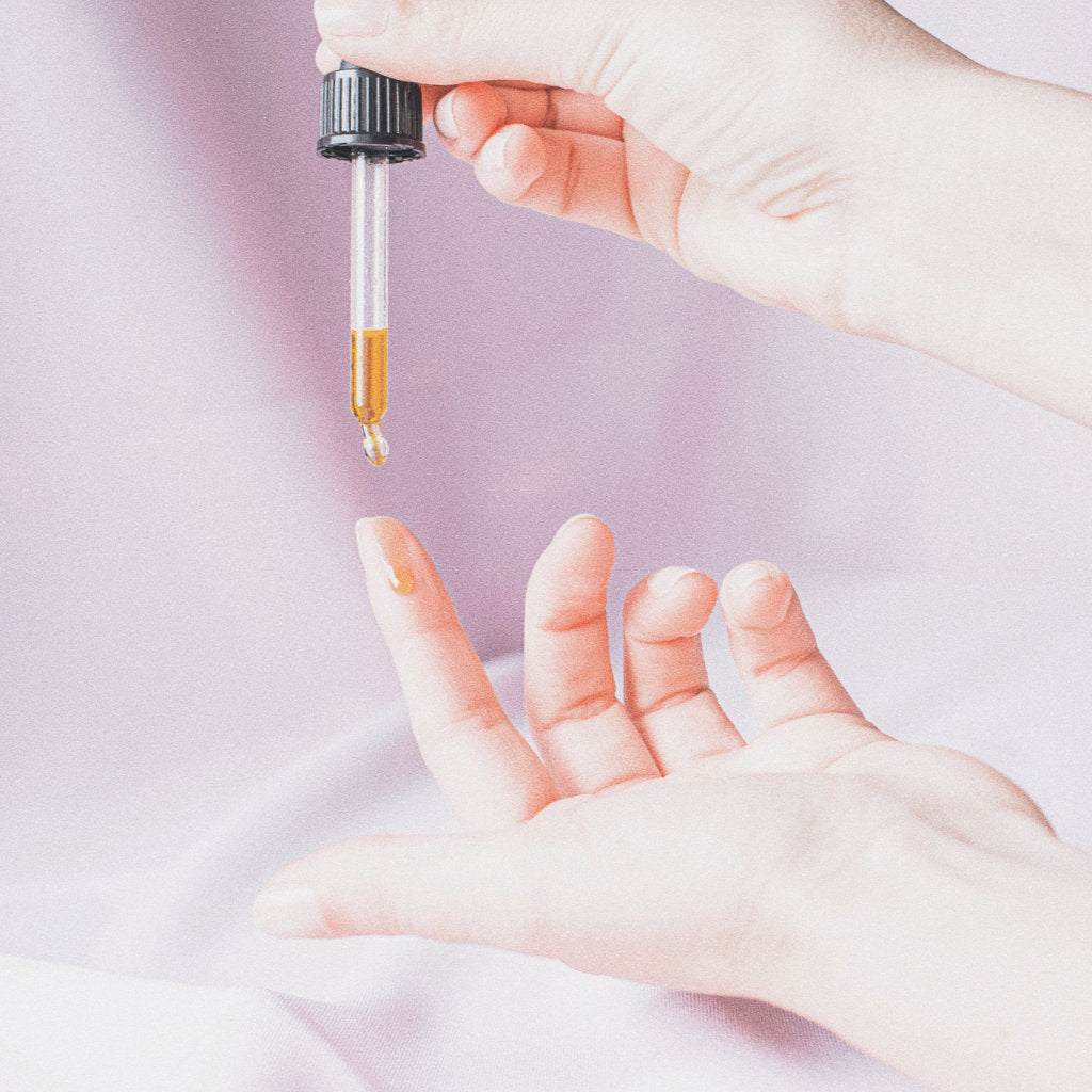 Hand holding a pipette with the Akasha blends Facial oil with golden colour dripping on a finger