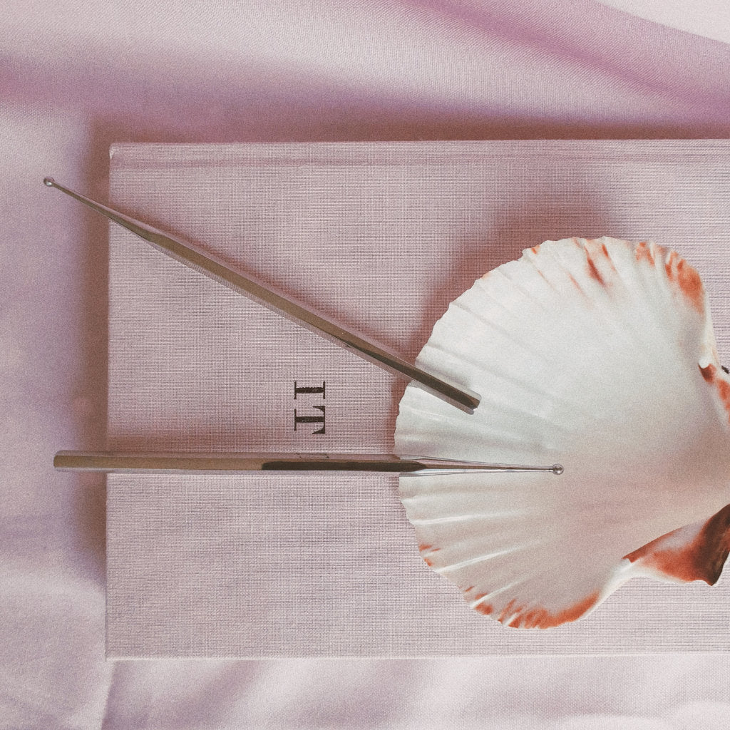 Two Facial reflexology tools on a shell with pink background
