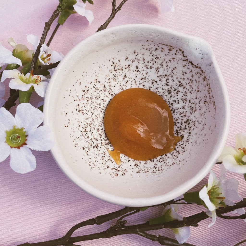 Some Manuka honey in an Akasha blends blow, on a pink background with a Manuka flower