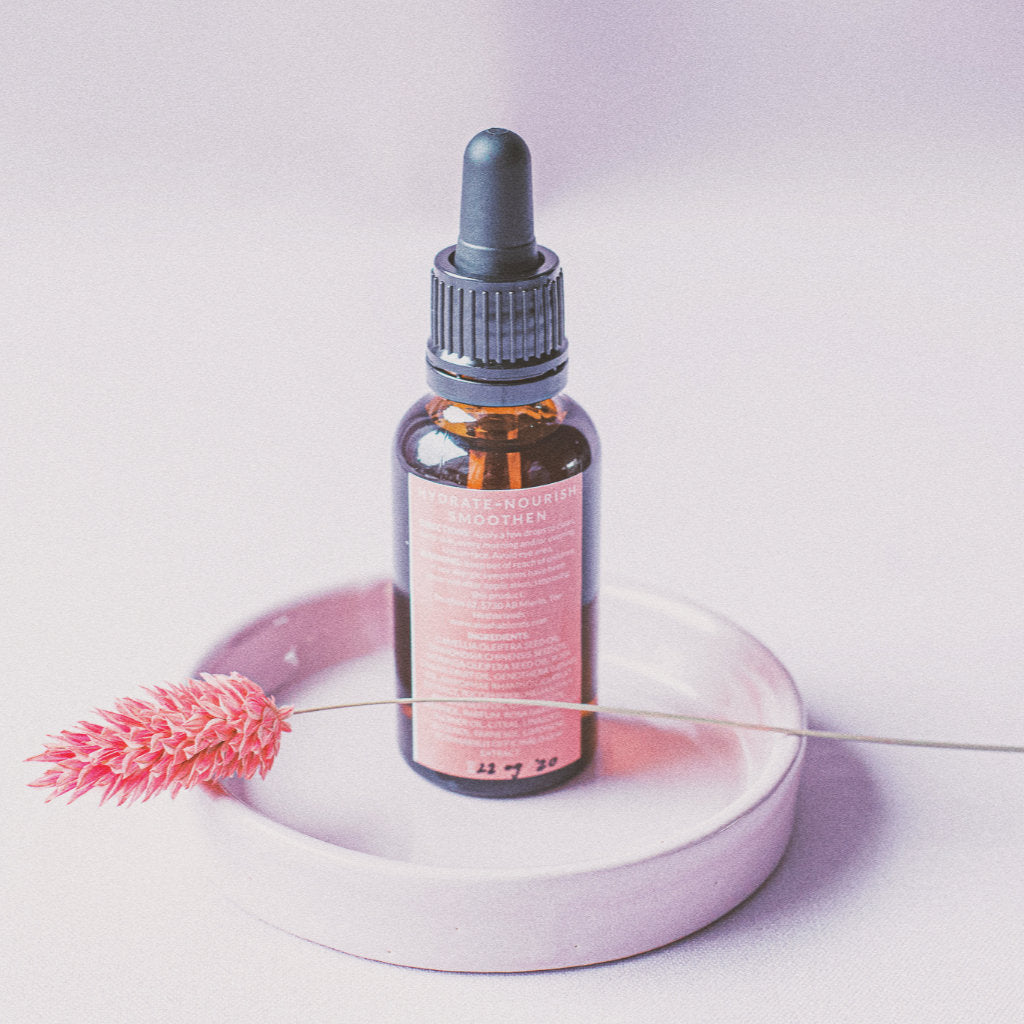 Facial oil Rose bottle on a pink plate with a piece of dry flower